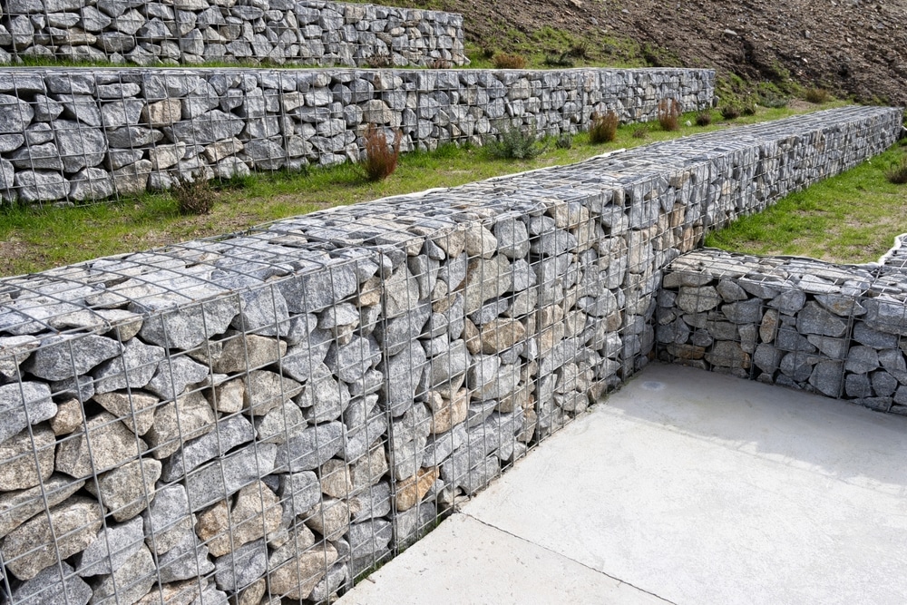 Murs de soutènement en gabions faits de cages métalliques remplies de pierres grises sur un terrain en pente.